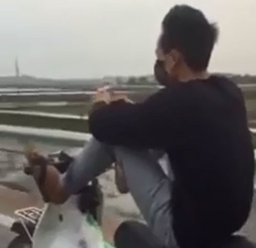 Thanh niên đầu trần vừa lái xe máy bằng chân vừa bấm điện thoại